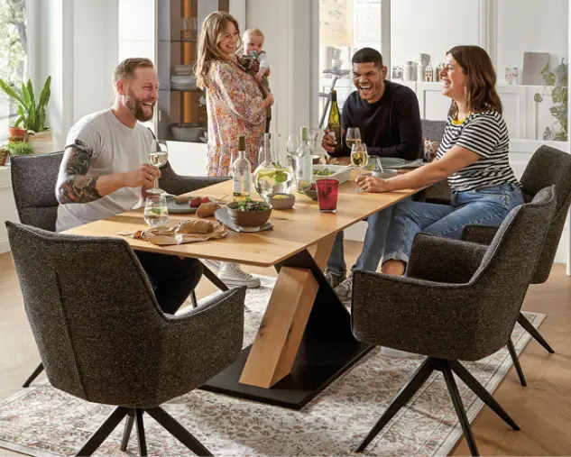 Helles Wohnzimmer mit zwei beigen Sofas, schwarzem Couchtisch, rotem Teppich und grüner Wand. Pflanzen, Regal und Stehleuchte schaffen ein modernes Wohnambiente mit gemütlicher Atmosphäre und natürlicher Raumgestaltung.